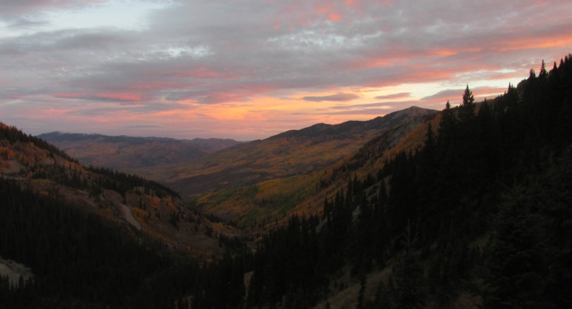 The sky appears in soft shades of pink, purple and orange as the sun sets or rises on a mountainous landscape